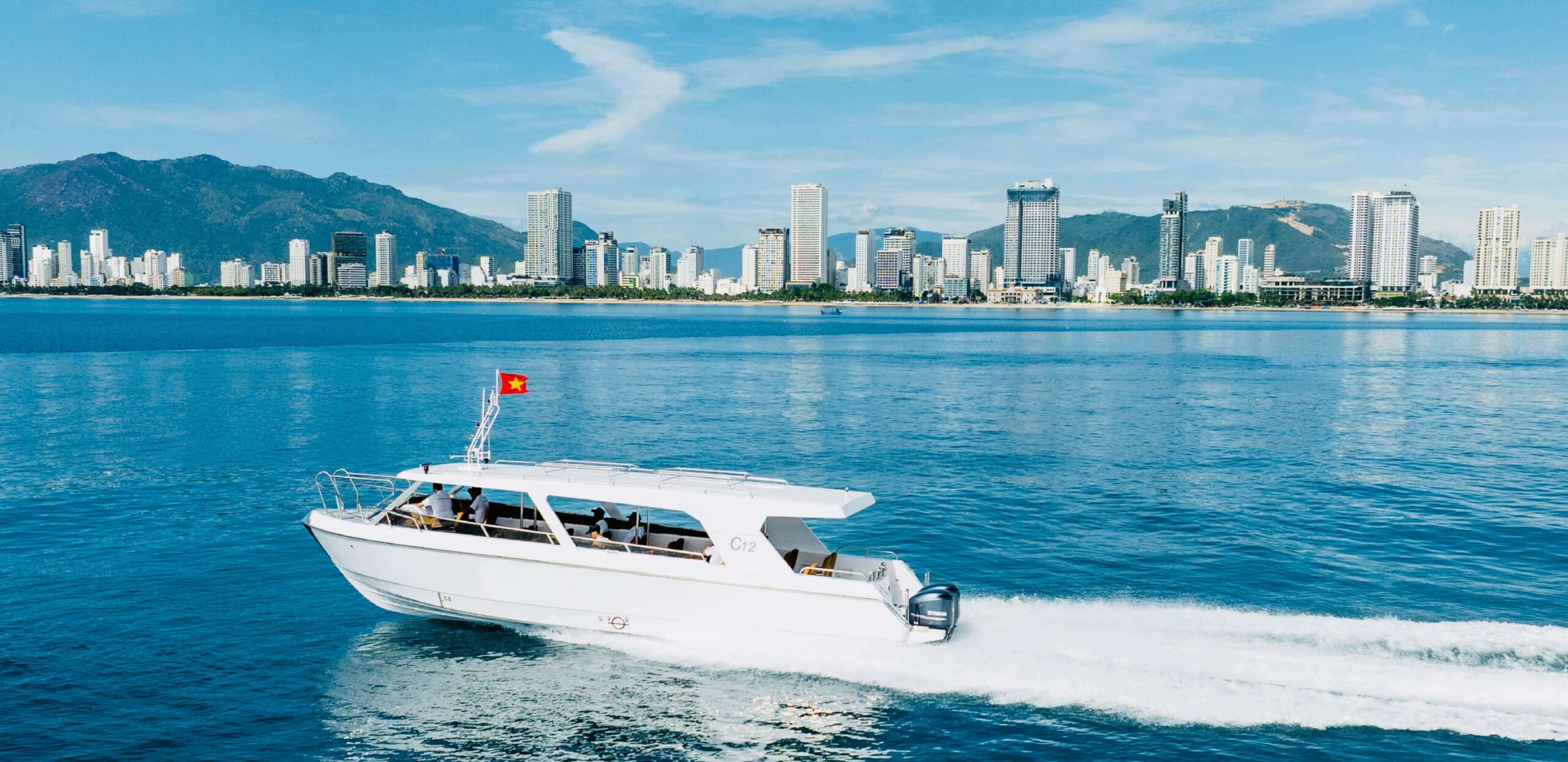 Tàu khách C12 Song Lo Boat chạy gần thành phố ven biển, phù hợp tuyến vận tải hành khách đảo. C12 passenger boat by Song Lo Boat cruising near coastal skyline, perfect for island passenger routes.